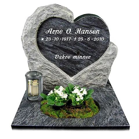 Gravstein formet som et hjerte i mørk stein med innfelt navn, lyslykt og hvite blomster foran.